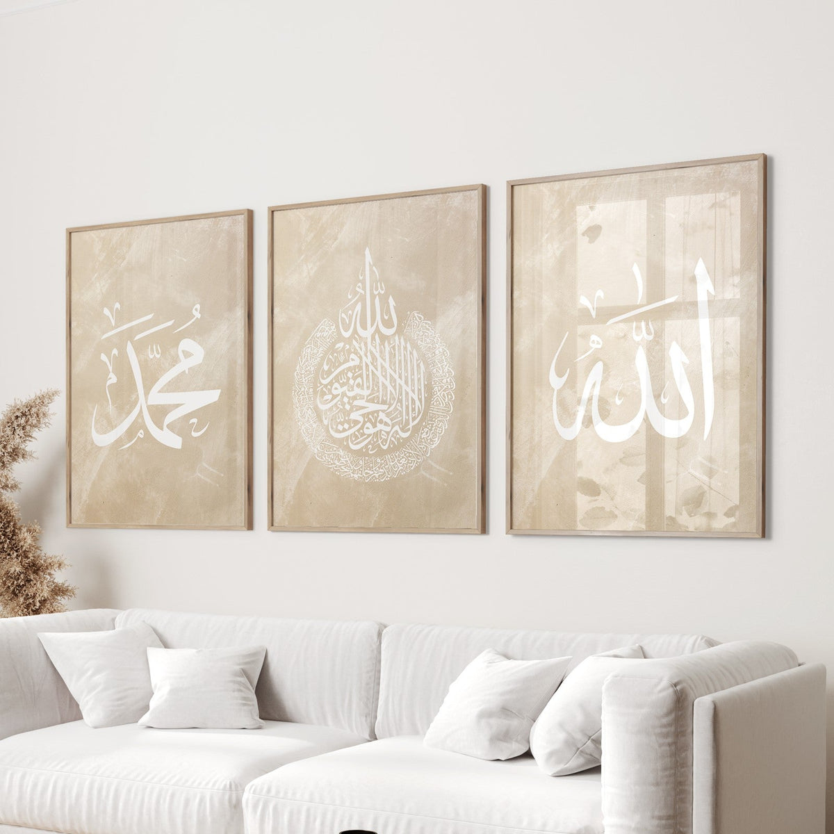 A set of three beige and white Islamic wall art prints featuring text in Arabic script, displayed above a white sofa, with a round wooden side table in the foreground.