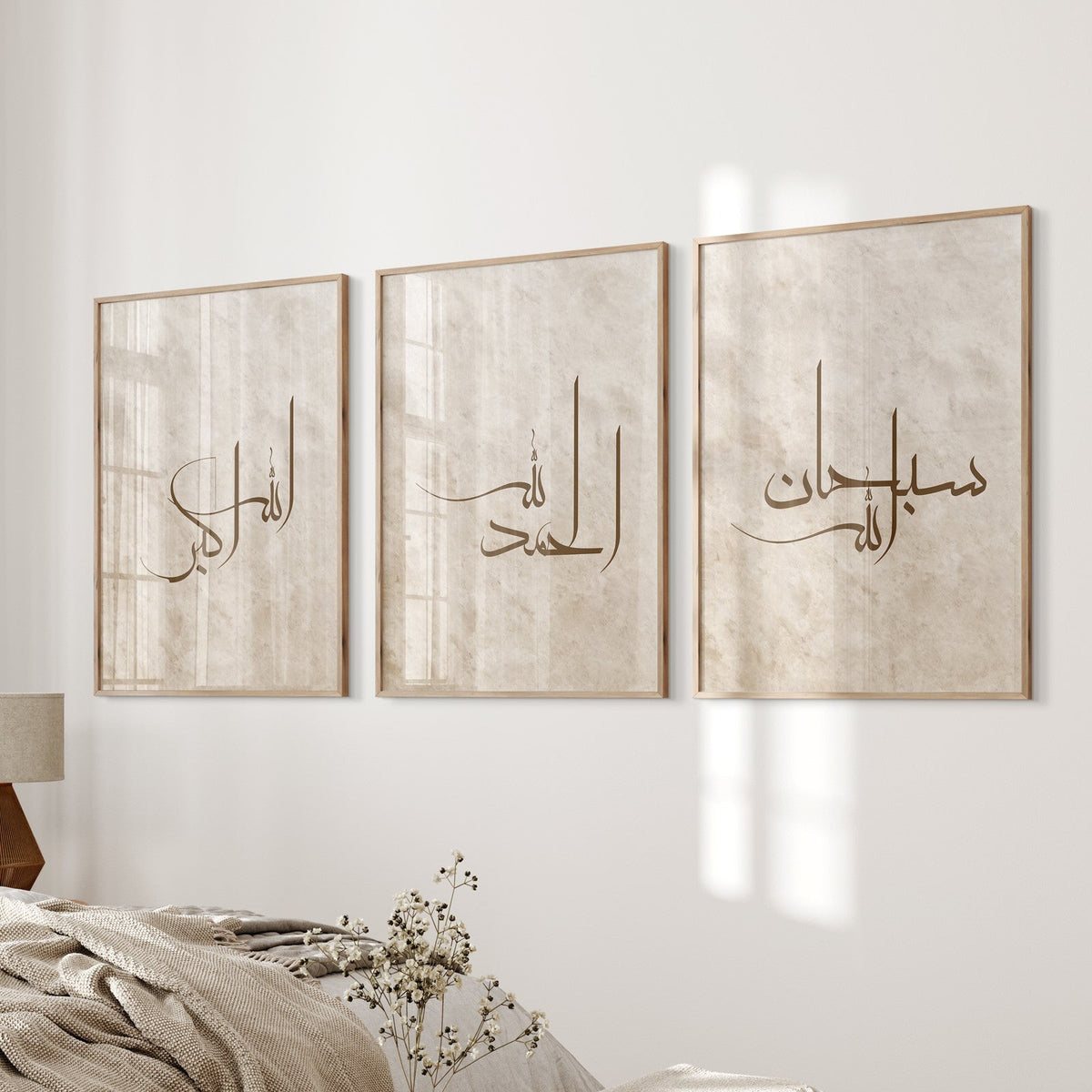 A set of three beige and brown framed wall art prints with Arabic calligraphy hanging on a white wall above a beige sofa. The artwork features the phrases Subhanallah, Alhamdulillah, and Allahu Akbar.