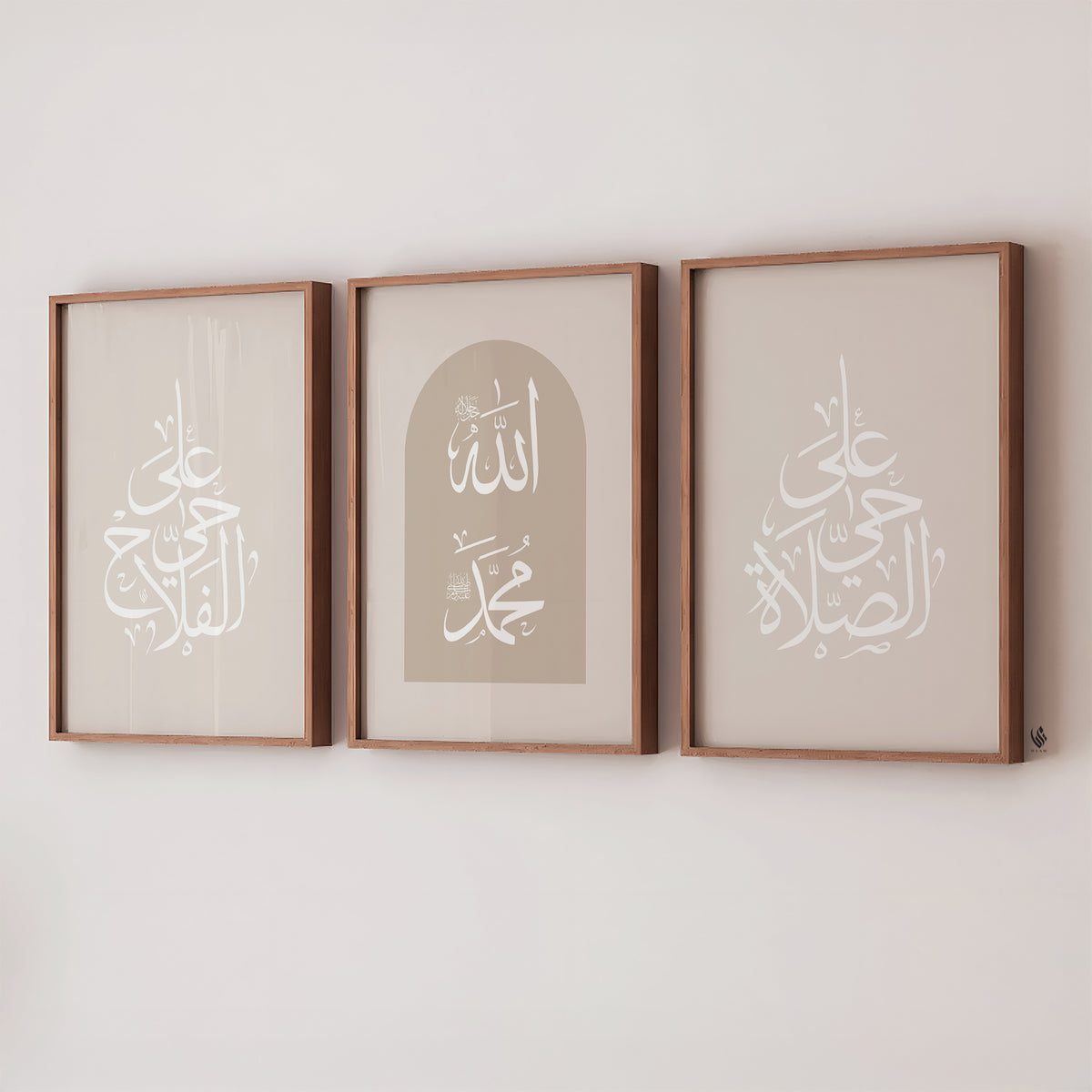 A set of three beige-framed Islamic wall art pieces is placed above a shelf with pillows, featuring Arabic calligraphy that reads "Hayya alasalah" and "Haya alal falah," which translates to "Come to prayer" and "Come to success," respectively, along with the names of Allah and Prophet Muhammad saw.