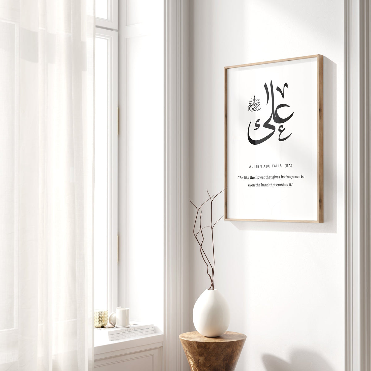Framed Arabic calligraphy artwork on a white wall with a window and decorative vase in the foreground.