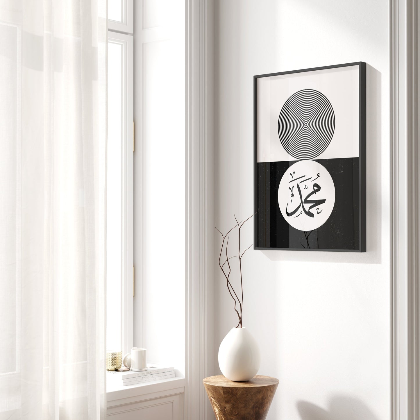 Framed black and white abstract art piece on a wall with a vase and plant below.