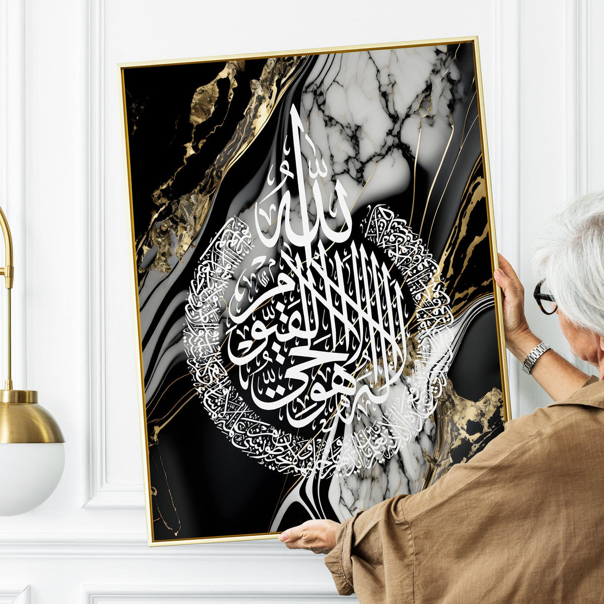 Person holding a framed artwork with Arabic calligraphy against a white wall.