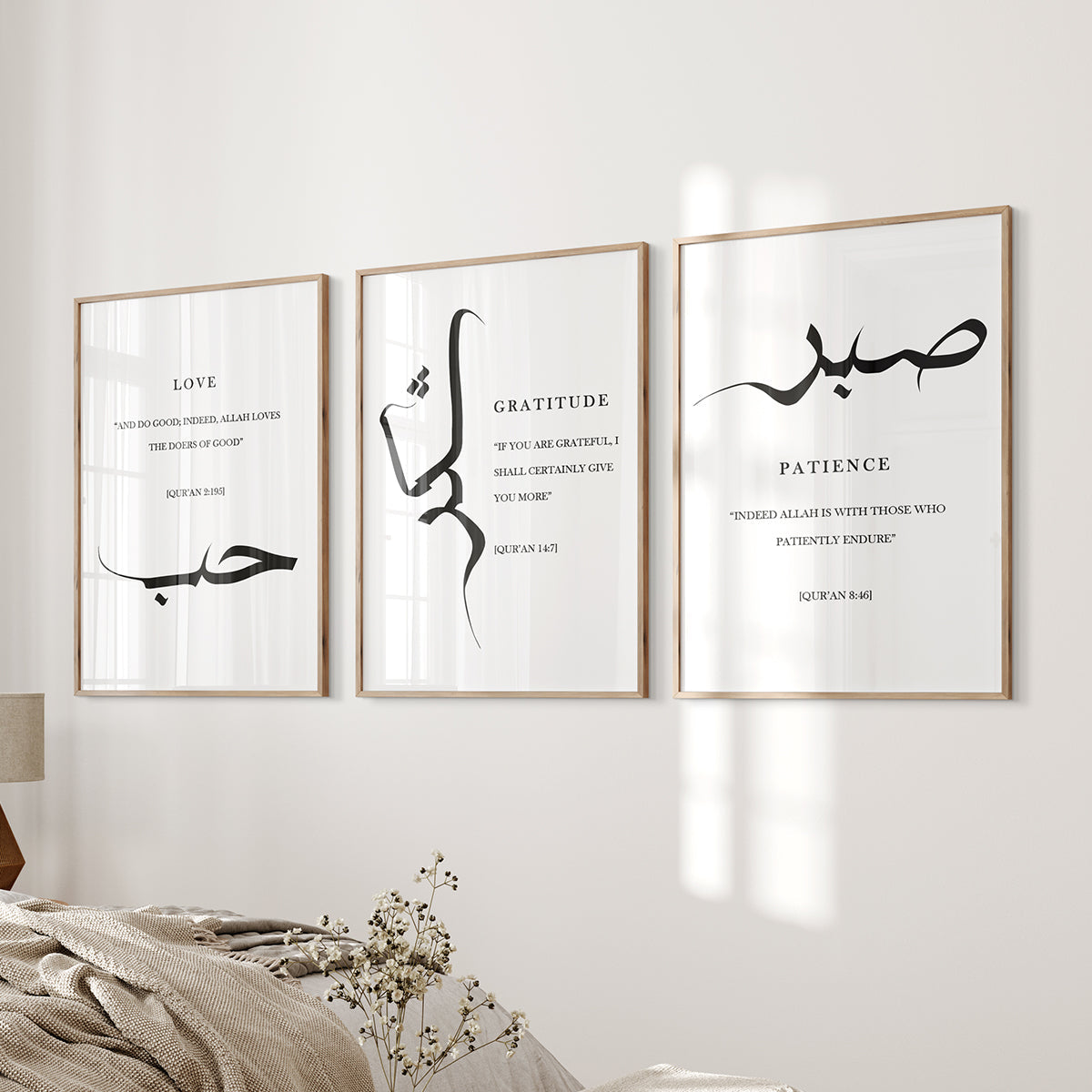 A set of three white Islamic wall art prints with black text Sabr Shukr and hubb in Arabic calligraphy, displayed above a bed in a room.