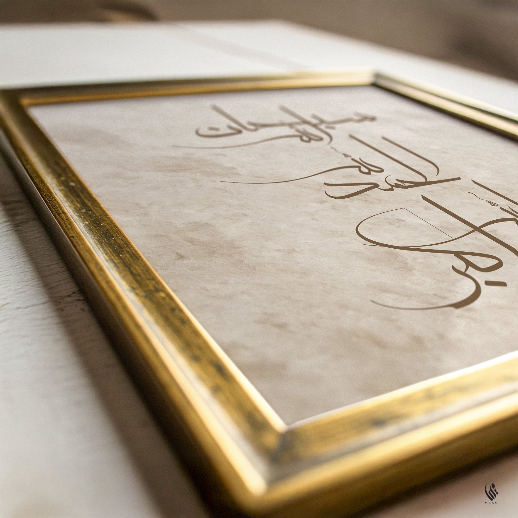 A framed piece of Arabic calligraphy art print with elegant gold-leaf lettering on textured beige paper, set in a rustic white wooden frame with a polished gold brass border.
