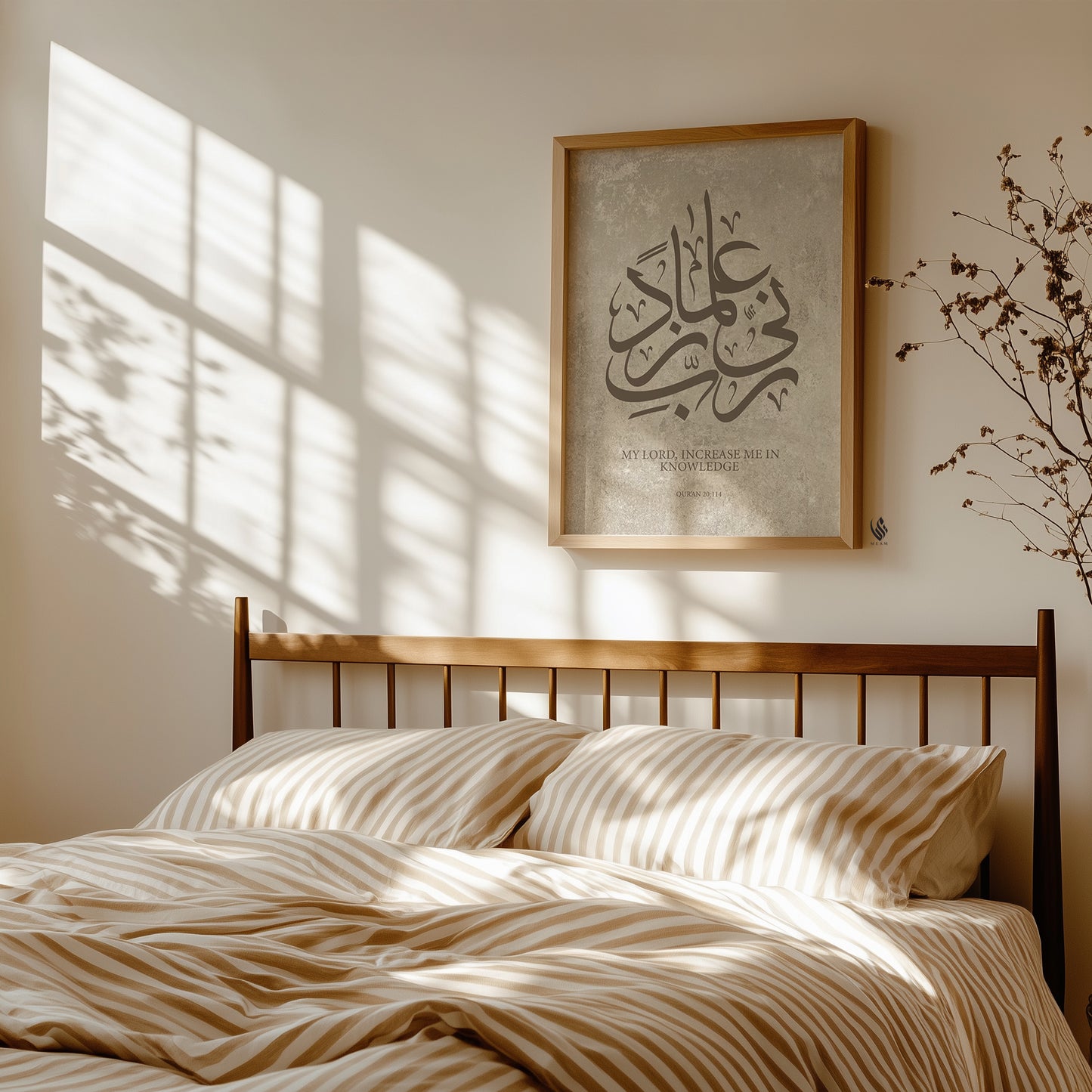 Minimalist bedroom interior with beige striped bedding and warm sunlight casting window shadows, featuring a framed Islamic wall art print with Arabic calligraphy “Rabbi Zidni Ilma” on a soft stone-textured background in neutral tones.