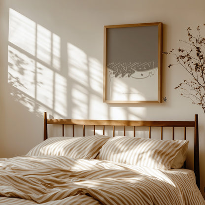 Bedroom with wooden headboard, striped bedding, and framed artwork on the wall. La'in shakartum Quran print displayed above a bed, soft beige tones against a white wall