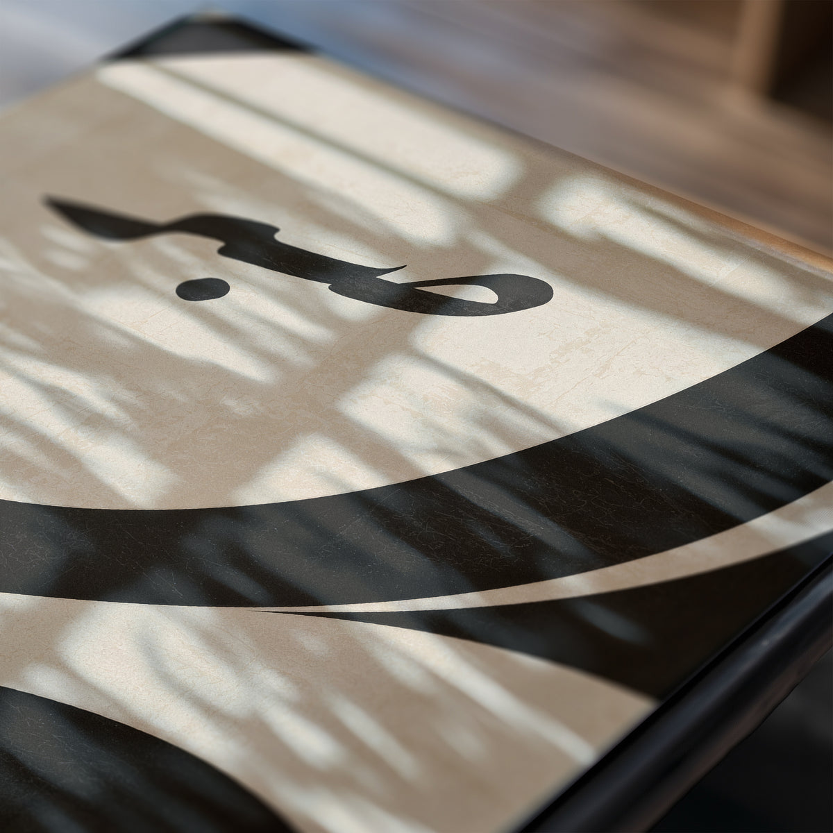 A close-up of a rectangular tray or plate with an abstract black and beige design, photographed in soft natural light with dappled shadows across the surface.