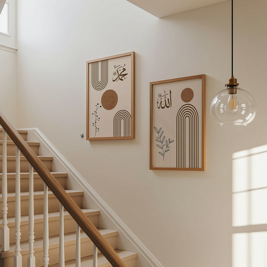 Two framed abstract Arabic calligraphy wall art prints with beige, brown, and black geometric designs hang on a cream-colored wall next to a wooden staircase and a hanging glass pendant light.