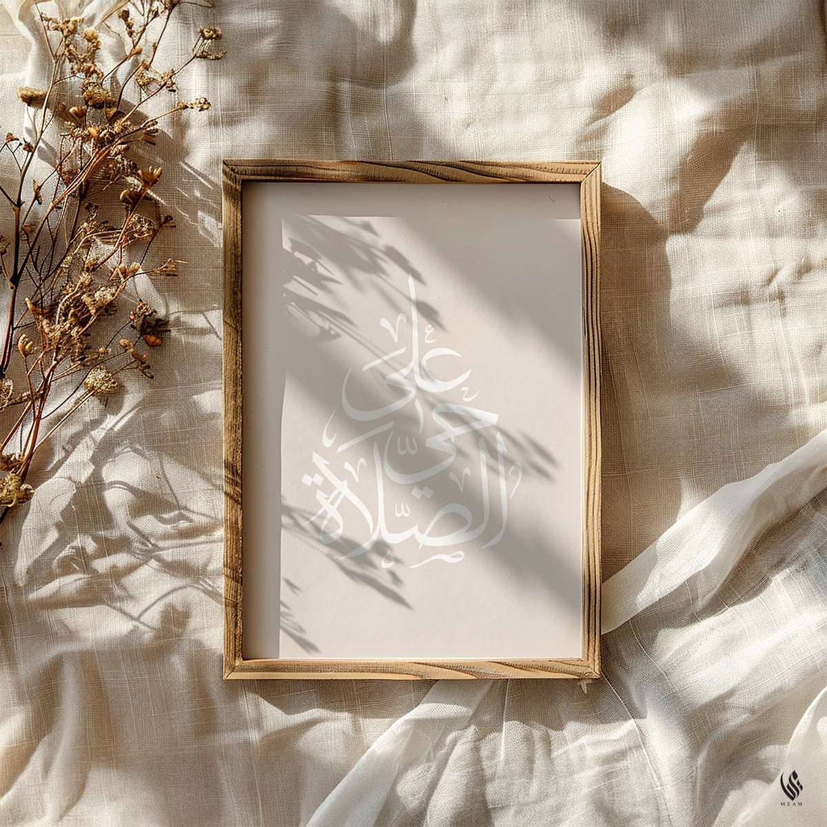 Neutral Islamic wall art in a wood frame featuring white Adhan Arabic calligraphy arranged in a pearl drop shape, styled on soft beige linen in sunlight.