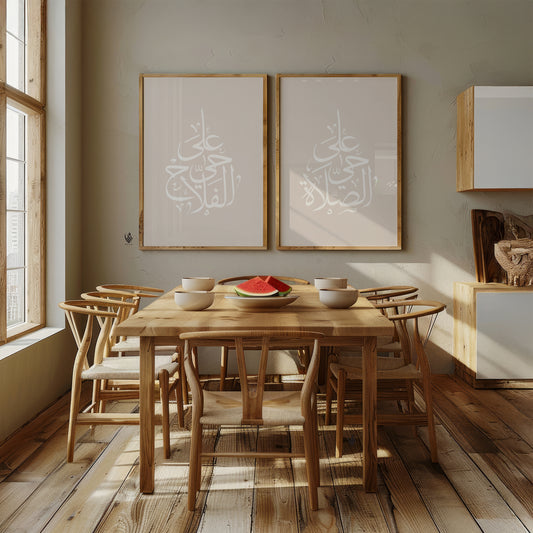 Set of 2 neutral Islamic wall art prints above a wooden dining table, featuring white Adhan Arabic calligraphy in elegant pearl drop-shaped compositions.