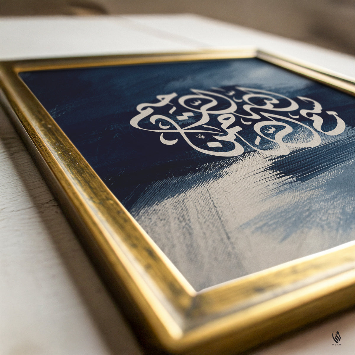 Close-up of Bismillah Arabic calligraphy in a gold frame, featuring cream script over deep navy, slate blue and textured abstract brushstrokes.