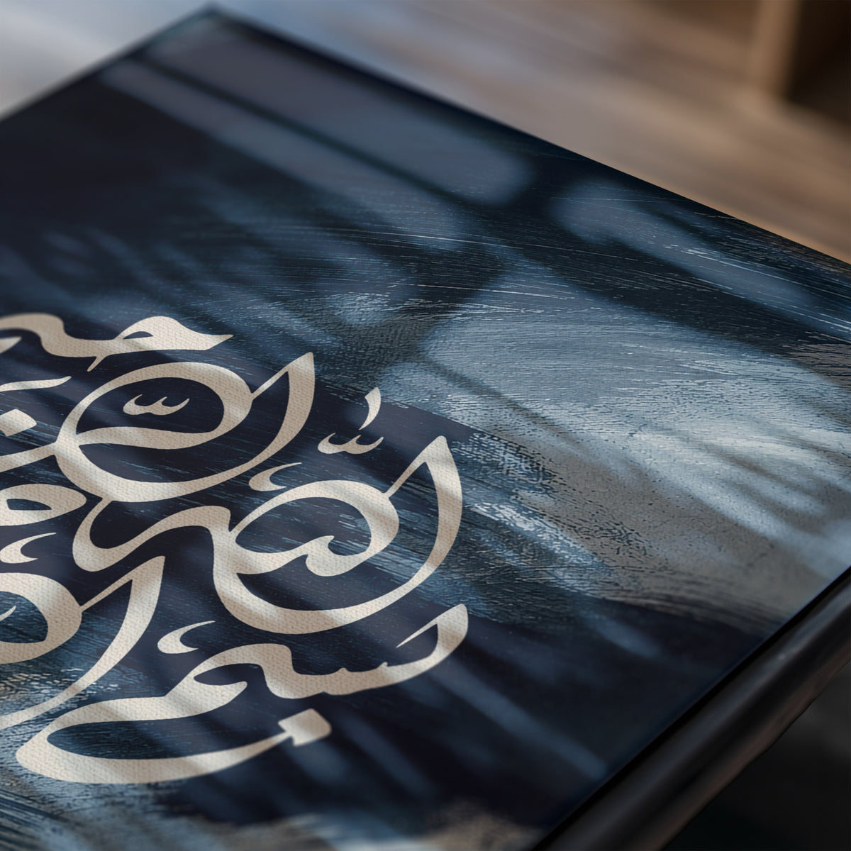 Detailed close-up of the Bismillah print showing cream Arabic calligraphy over navy and smoky blue painterly texture with soft window reflections.