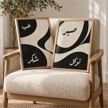 Set of two black and beige Islamic wall art prints with Arabic calligraphy, displayed in wooden frames on a cream boucle chair beside a tall olive tree in a warm neutral interior with soft natural light and modern decor.