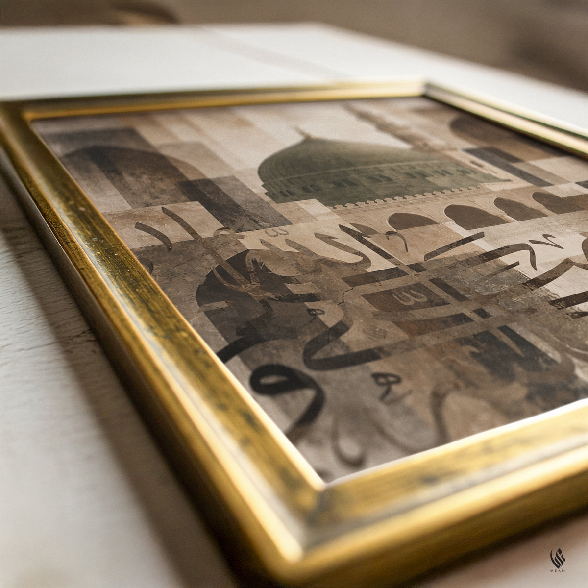 A framed art print featuring a sepia-toned collage of architectural domes and Arabic calligraphy, housed in a distressed gold frame, resting on a light-colored wooden surface.