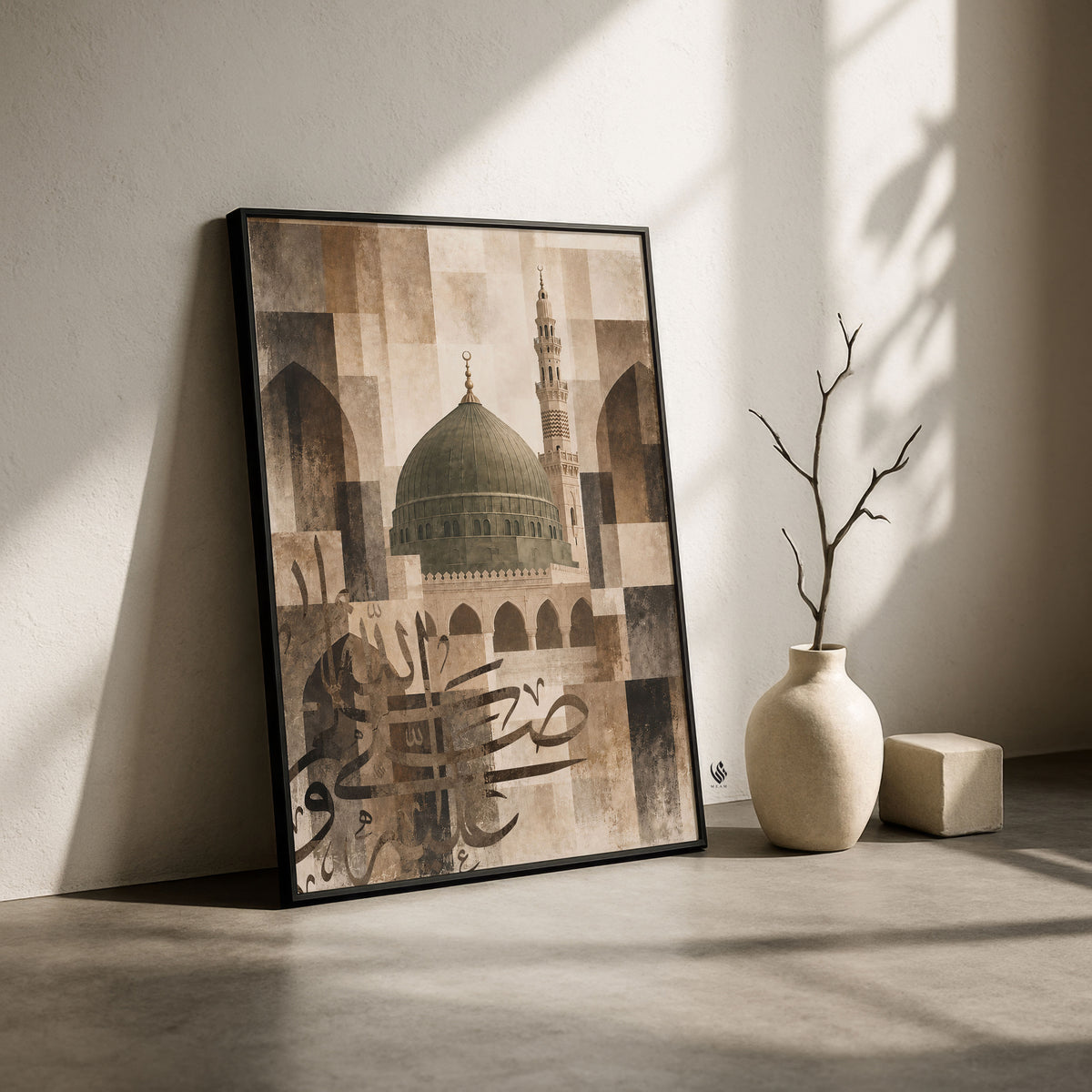 Black-framed Madina mosque artwork leaning against a minimalist wall with beige ceramics and strong natural shadows.