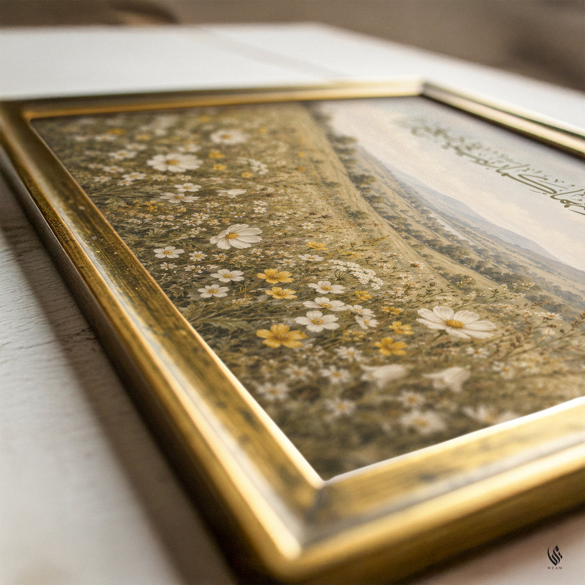 Angled close-up of a gold picture frame surrounding the printed botanical meadow, showing tiny daisies, warm yellow blossoms, gentle hills and part of the Arabic lettering.